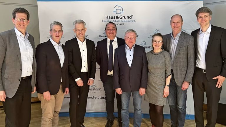 Acht Personen stehen vor einem Haus und einem Grundstücks-Plakat und schauen in die Kamera. In der Mitte steht Geschäftsführer Herr König vom EBZ.