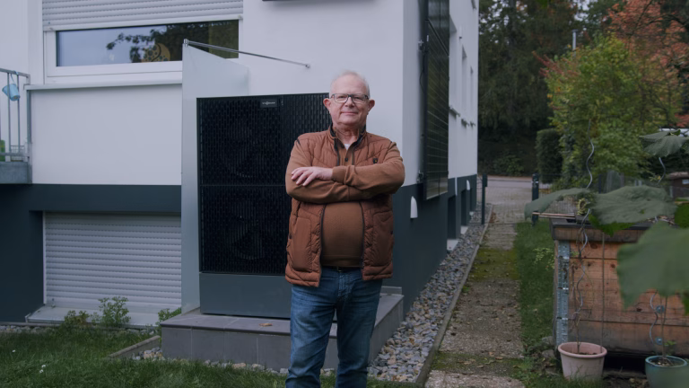 ein Mann steht mit verschränkten Armen stolz vor seiner Wärmepumpe im Garten