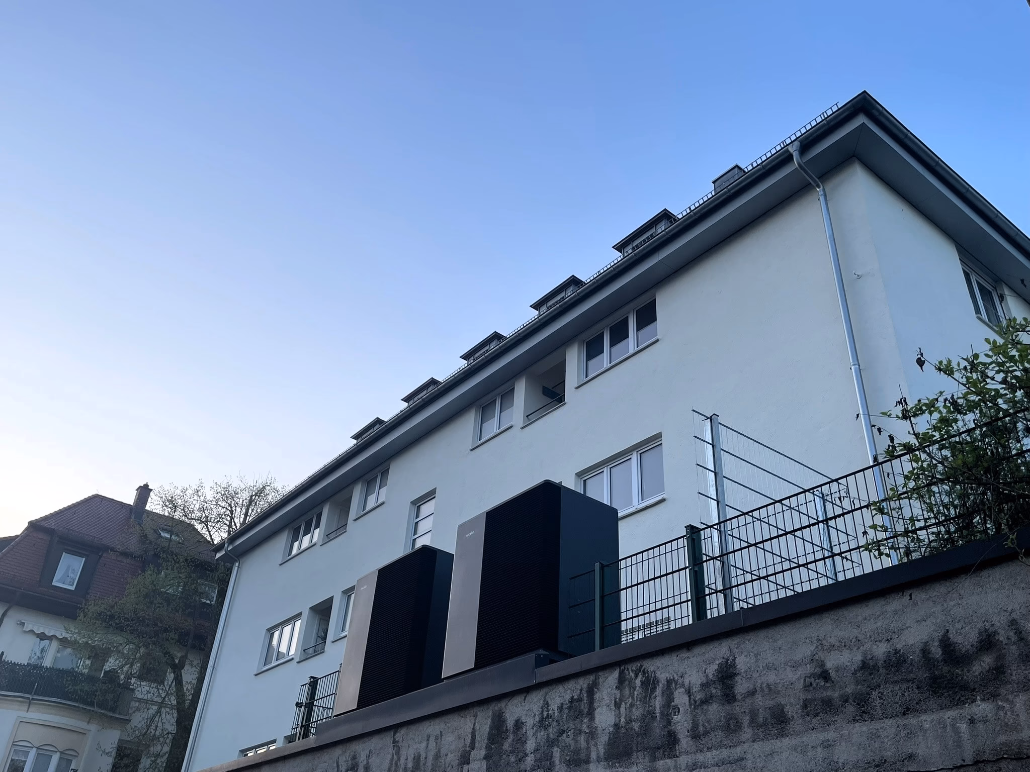 zwei große Wärmepumpen vor einem Mehrfamilienhaus