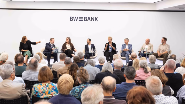 8 Menschen sitzen auf dem Podium vor einem großen Publikum in der BW-Bank
